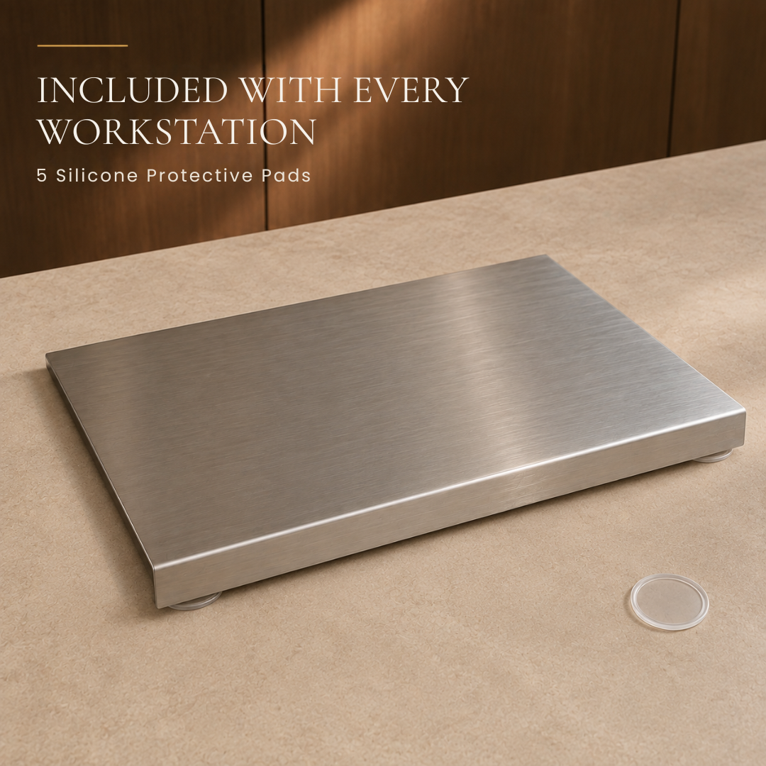 A brushed stainless steel rectangular desk scale or platform shown on a beige countertop, with overlaid text reading 'INCLUDED WITH EVERY WORKSTATION' and '5 Silicone Protective Pads.' A small clear silicone pad is placed nearby on the counter.
